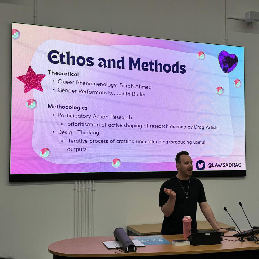 One of our researchers, James, stood in front of a colourful powerpoint slide containing some information on our ethos and methods