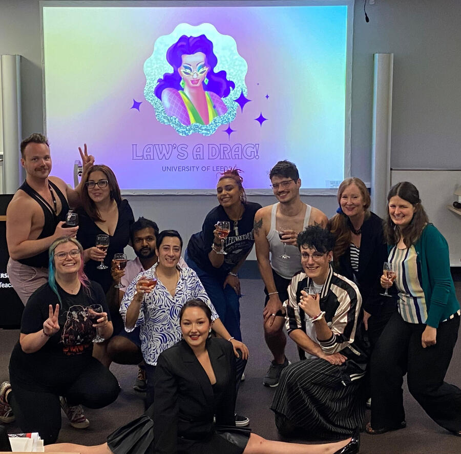 A group of participants and researchers at one of our events taking a selfie in front of the law's a drag logo whilst holding glasses of wine